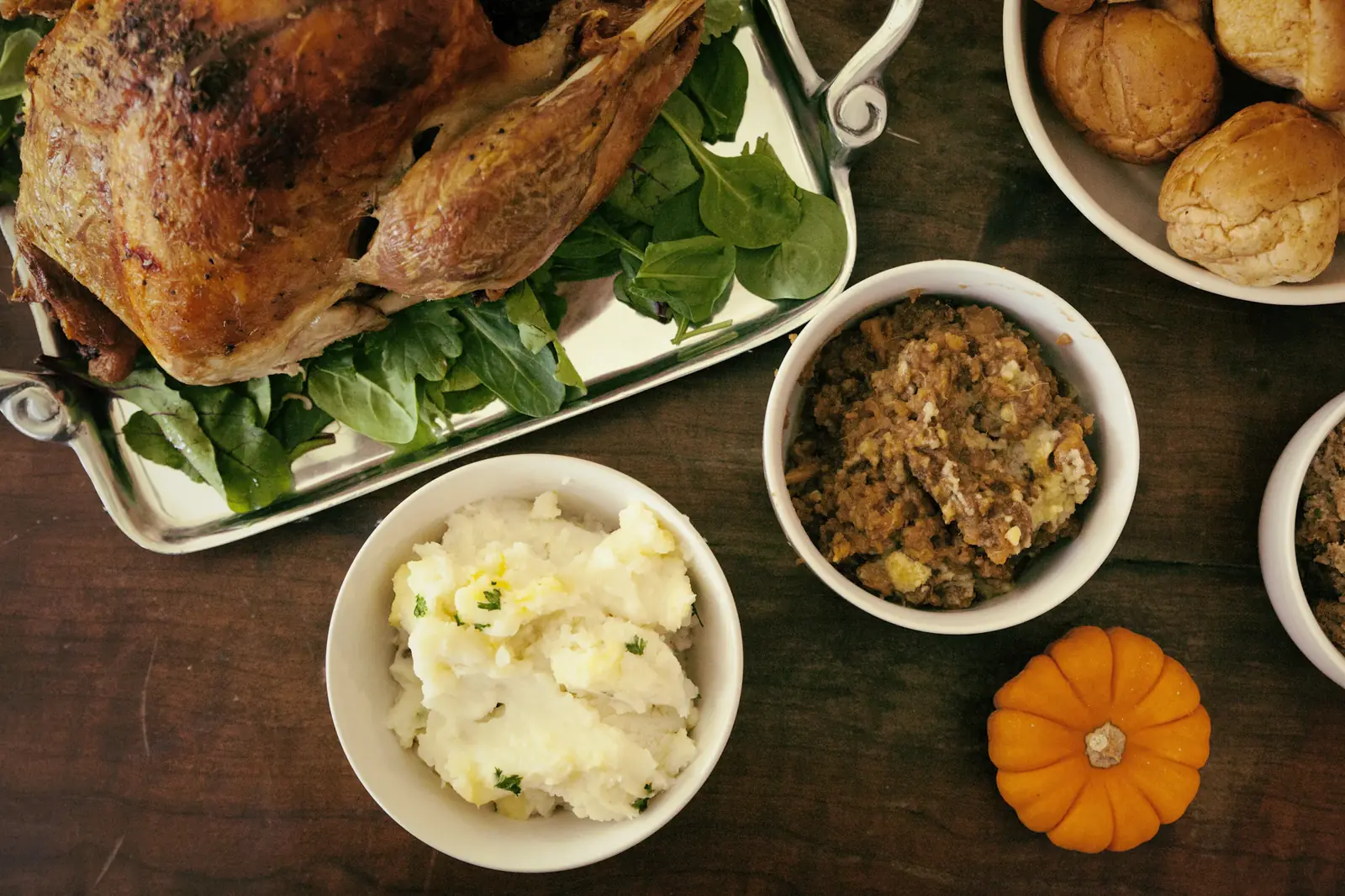 A roast turkey with mashed potatoes, stuffing and rolls on a wooden table